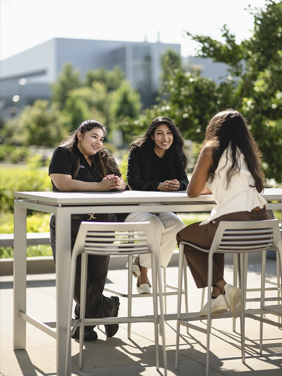 Three students talk outside at a table