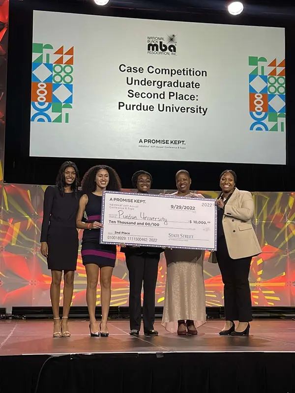Labi stands with her partners holding a giant check for winning second place at NBMBAA