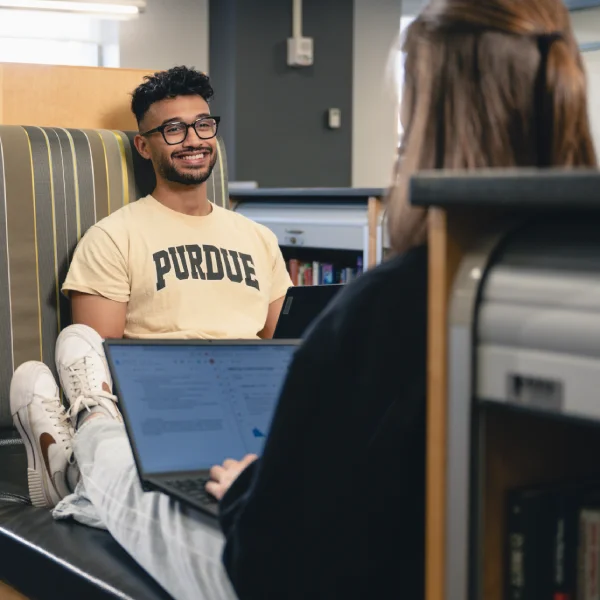 Two students in library discussing data on laptops